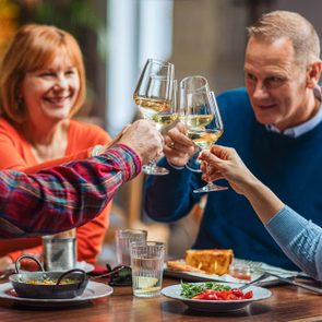People clink wine glasses, celebrating at a table with food in a cozy indoor setting.