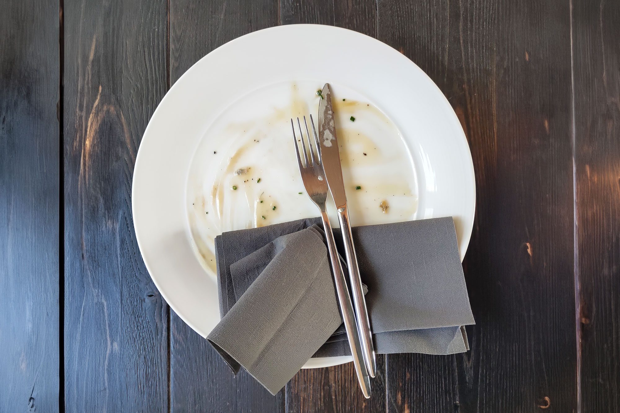 Dirty Plate And Textile Napkin With Fork And Knife On Wooden Table After Dinner
