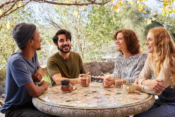Smiling young friends having coffee around a table outside