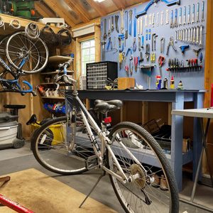 Bicycle stands in a well-organized workshop with tools on the wall and shelves filled with supplies in a wooden shed.