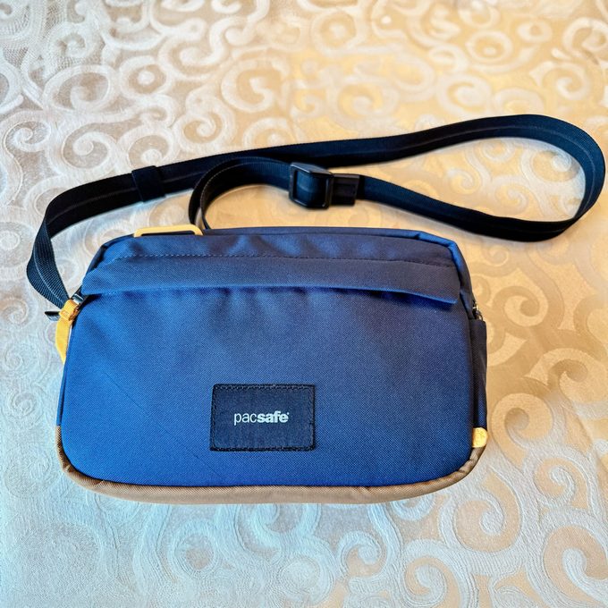 A blue shoulder bag rests on a patterned tablecloth, featuring a label with 