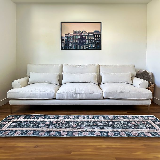 White sofa sits quietly against a wall with framed urban photo above; patterned rug lays on wooden floor in a minimalist room.