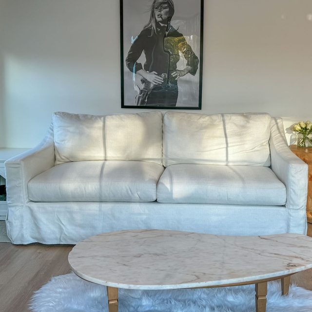 A white sofa sits in a room with a marble coffee table and a black-and-white portrait on the wall above it.