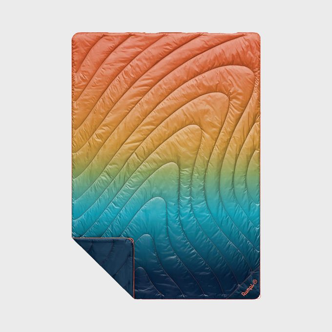 Quilt displaying gradient colors from orange to blue with wavy stitched patterns, slightly folded corner, on a plain background.