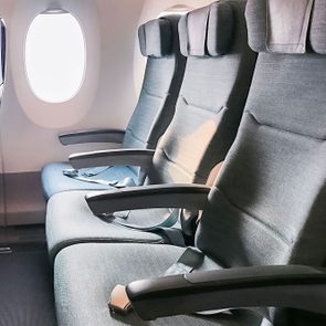 Three upholstered airplane seats sit empty; sunlight filters through a nearby window.