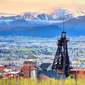 A mining structure stands tall amidst a town, with snow-capped mountains and a clear sky in the background.