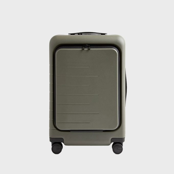 A green suitcase with four wheels stands upright; it has a rectangular design and a handle, set against a plain gray background.