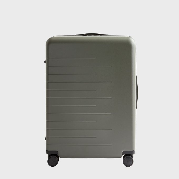 Green suitcase rests on wheels, displaying ridged texture in a minimal studio setting.