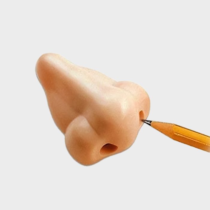 A pencil enters a nostril of a realistic fake nose against a plain gray background.