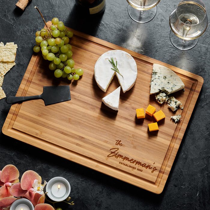 Cheese rests on a wooden board surrounded by grapes, flowers, and candles. Text reads 
