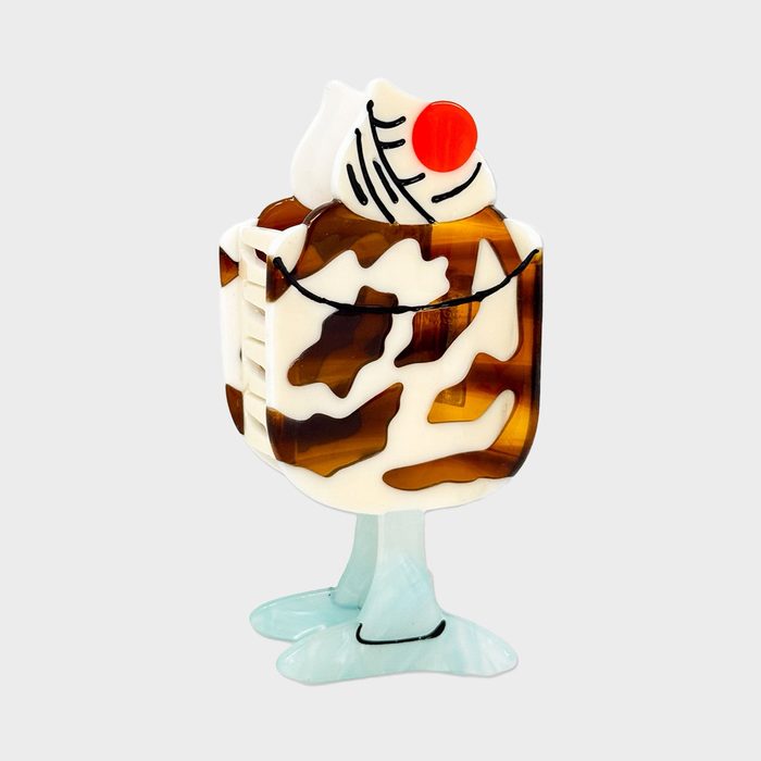 Plastic ice cream sundae brooch featuring chocolate swirls and a cherry, standing upright on duck-like blue feet, against a plain background.