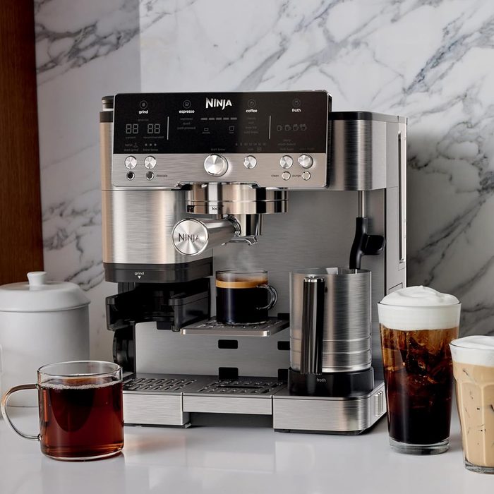Espresso machine brews coffee; compact kitchen setting; marble backsplash; cups of espresso, coffee, and milk froth nearby.