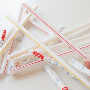 Hand holding a striped straw amidst scattered wrapped straws on a white surface.