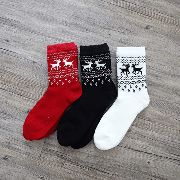 Three socks displayed on a wooden floor, featuring deer patterns, in red, black, and white colors.