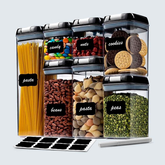 Plastic containers hold pasta, candy, nuts, cookies, beans, and peas; they sit on a surface with blank labels and a marker nearby.