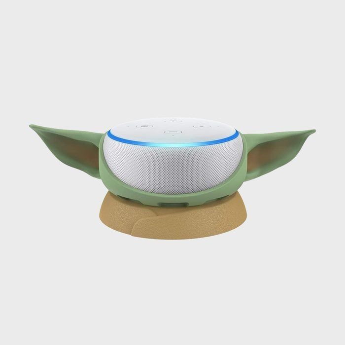 A smart speaker resembling a character with green ears rests on a brown base, set against a plain, light gray background.