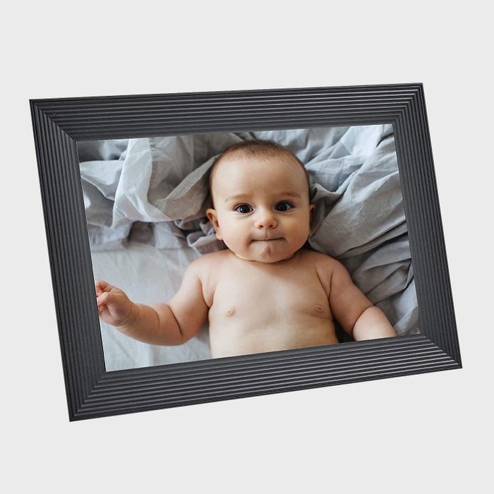A baby lies on grey sheets in a photo framed by a textured black border.