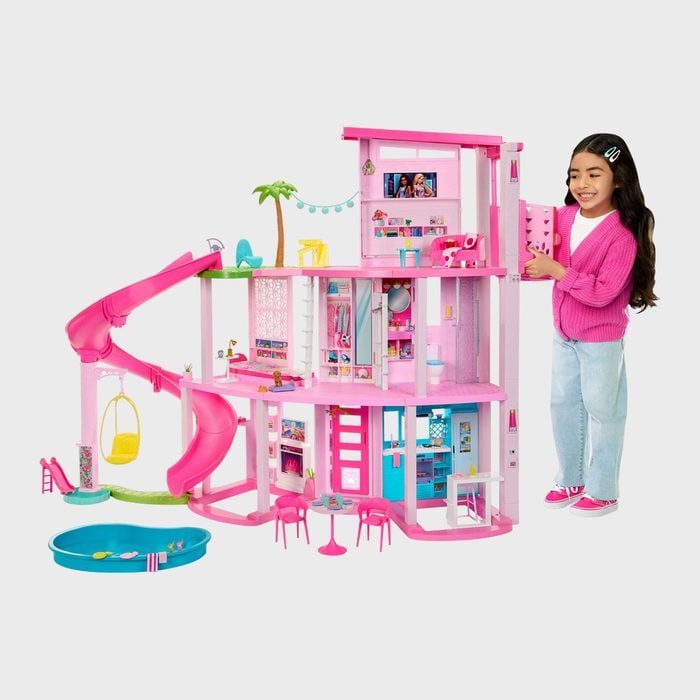 Dollhouse features multiple levels with pink slide, arranged in a child's playroom, alongside a happy child interacting with the set.