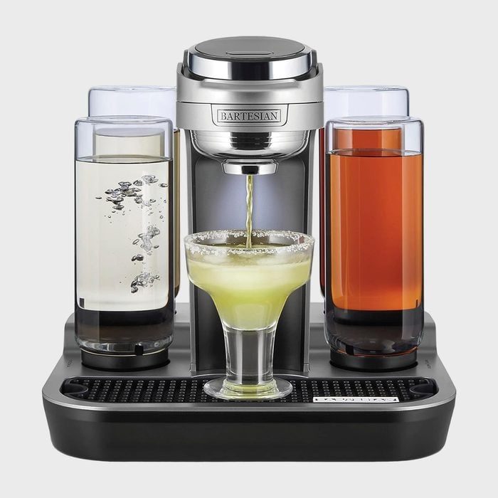 A cocktail machine dispenses a drink into a margarita glass, surrounded by four liquid-filled containers.