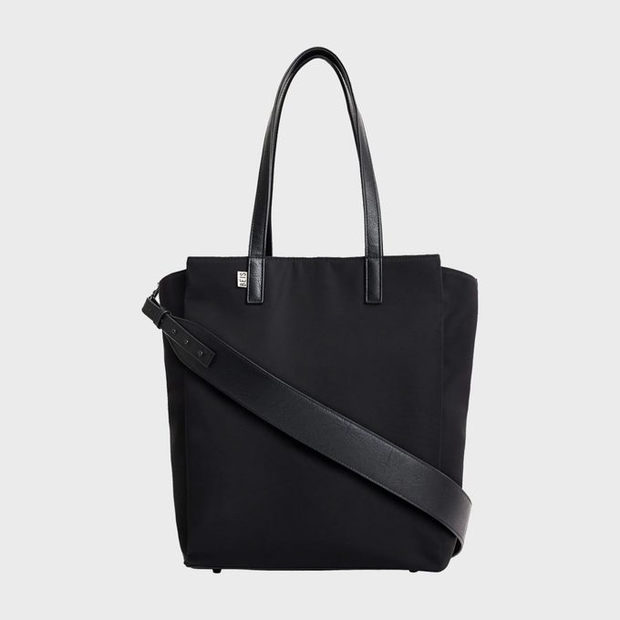 A black tote bag with dual handles and a crossbody strap, featuring a small logo tag, set against a white background.