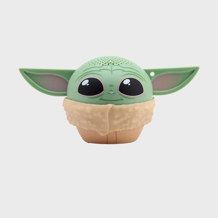 A small, green, baby alien-themed speaker sits against a plain, light gray background.