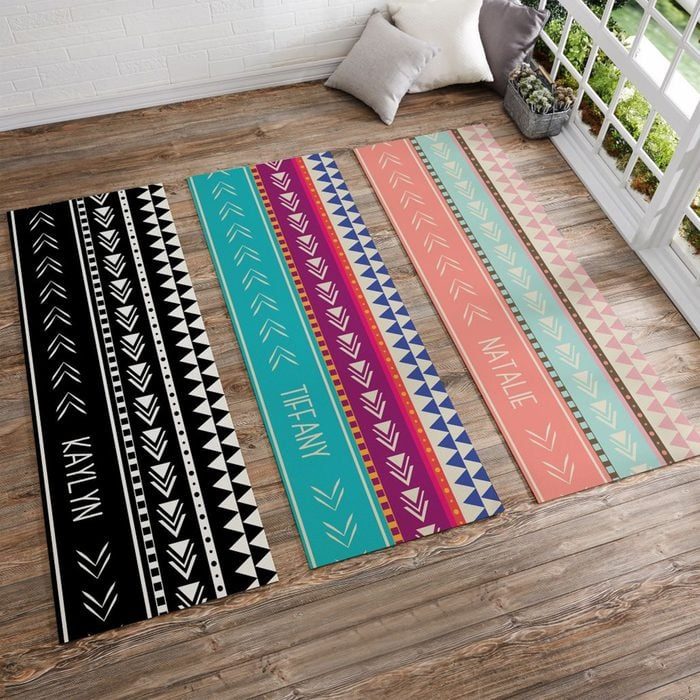 Rugs display geometric patterns and names, arranged on wooden floor near a window. Names include 