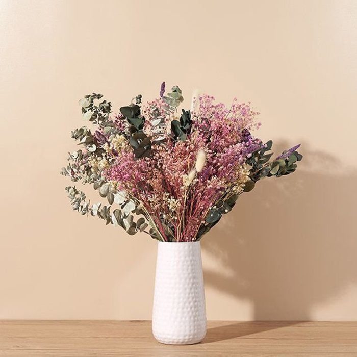 Flowers arranged in a white vase, placed on a wooden surface against a plain beige wall.