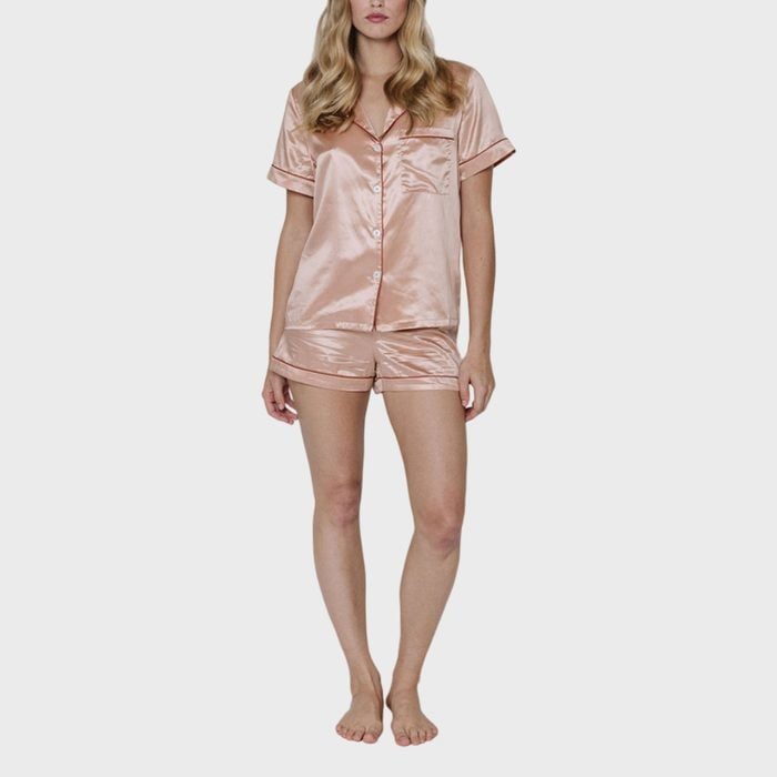 A person stands wearing a matching satin pajama set, consisting of a short-sleeved shirt and shorts, against a plain white background.