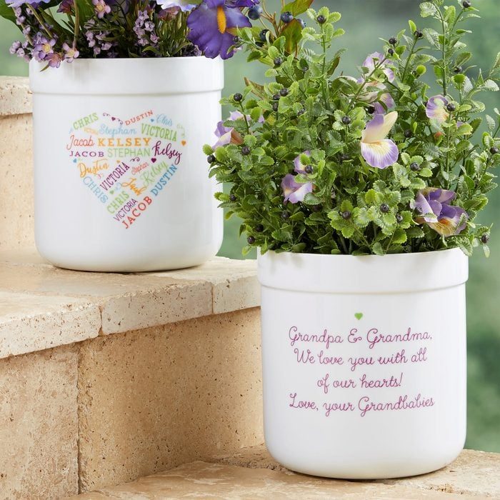 Potted flowers sit on steps, with personalized messages and names written on the pots, enhancing a heartfelt family connection in a garden setting.