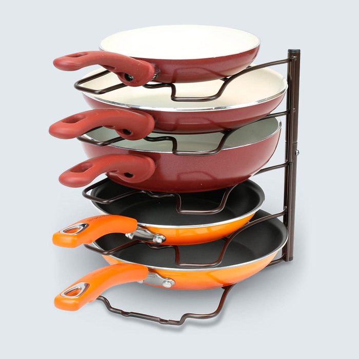 Five non-stick frying pans stack neatly on a vertical metal rack, showcasing different colored handles in a kitchen environment.