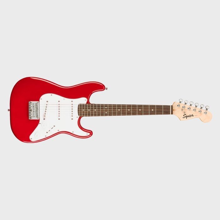 A red electric guitar with a white pickguard lies horizontally against a plain background; 