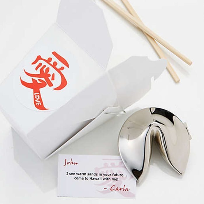 Metal fortune cookie lies beside an open takeout box labeled 