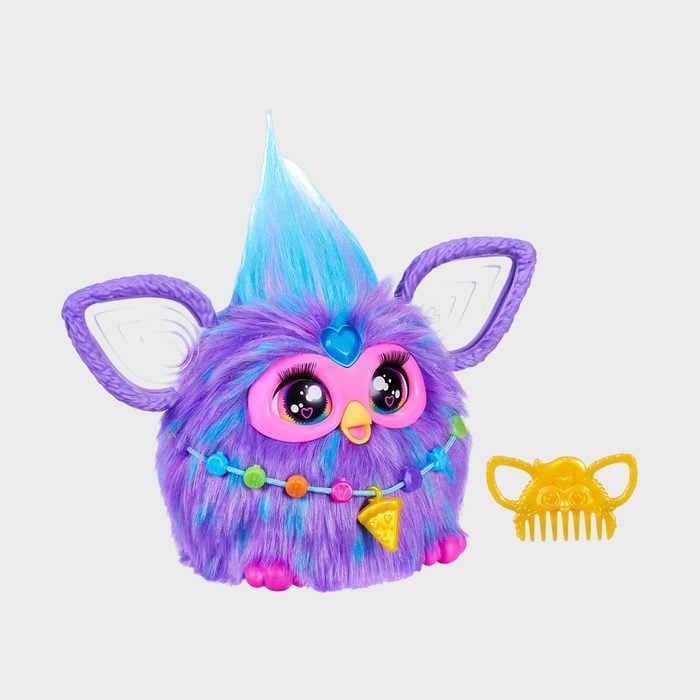 A colorful toy with blue fur, big eyes, and a decorative necklace sits beside a yellow comb in a plain background.