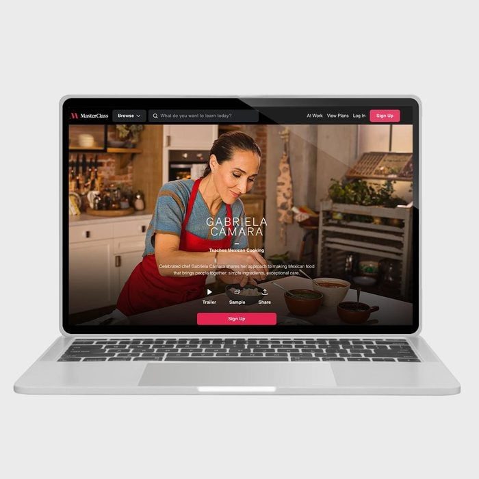 A laptop displays a cooking course featuring Gabriela Camara in a kitchen, with buttons for trailer, sample, share, and sign up.