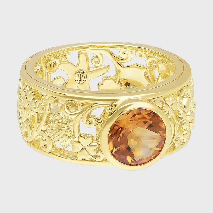Ornate gold ring displays an intricate floral pattern, featuring a prominent, round amber gemstone, set against a plain light background.