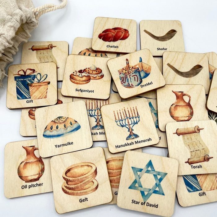 Wooden cards display Jewish symbols and words (e.g., Challah, Shofar, Dreidel) scattered around a table, with a cloth bag nearby.