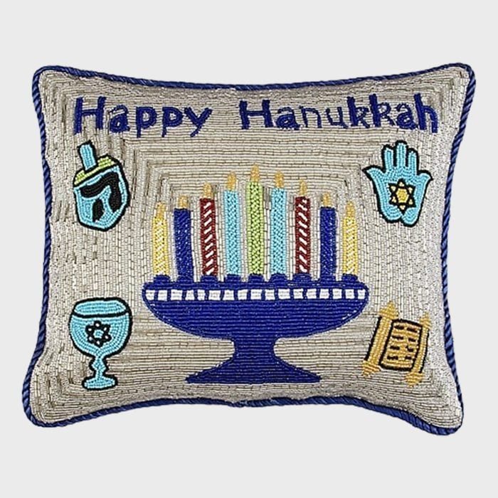 Pillow features a menorah with candles set on silver fabric, surrounded by a dreidel, chalice, hamsa, and scroll. Text reads â€œHappy Hanukkah.â€