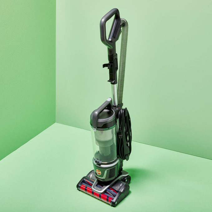 Upright vacuum cleaner standing still in a corner of a light green room.