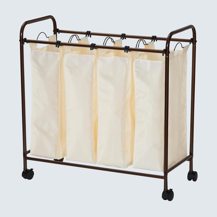 Laundry sorter with four cream-colored fabric bags hanging, supported by a brown metal frame on wheels, against a light gray background.