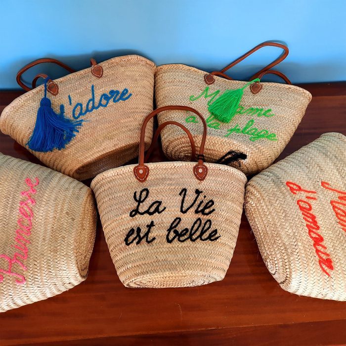 Woven baskets lie on a wooden surface, each adorned with colorful tassels and French text: 