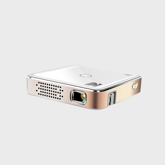 Projector sits idle; sleek, metallic design with lens and ventilation openings, placed against a plain, light background.