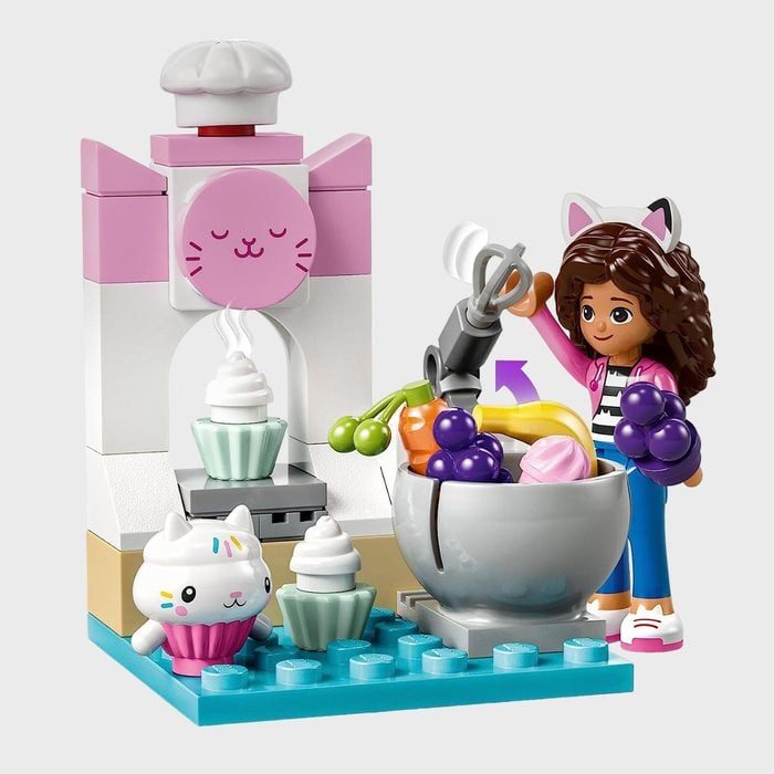 Toy kitchen set features a figure mixing fruits in a bowl beside desserts and a cat-themed dessert machine with colorful, whimsical design elements.
