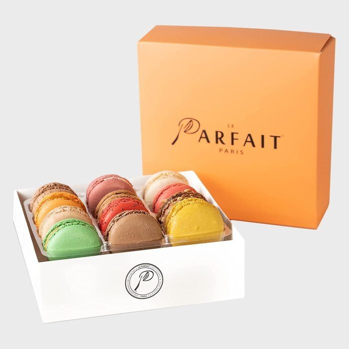 Macarons are arranged in a row inside a white box, presented with an orange box labeled 