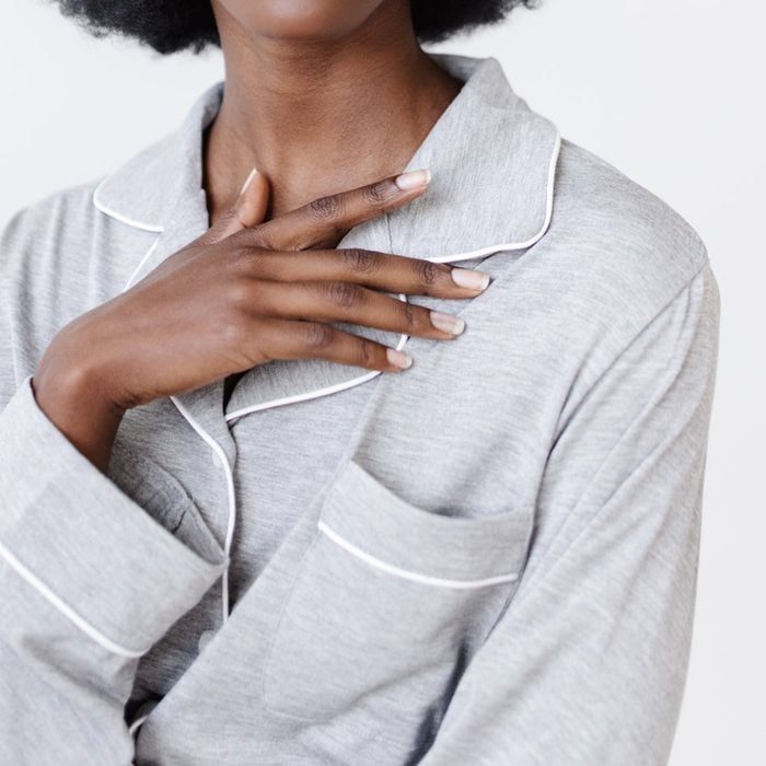 A hand rests on a gray, collared pajama top with white piping, set against a plain background.