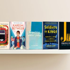 Five books are lined up on a white shelf against a beige wall, displaying various colorful cover designs and titles.