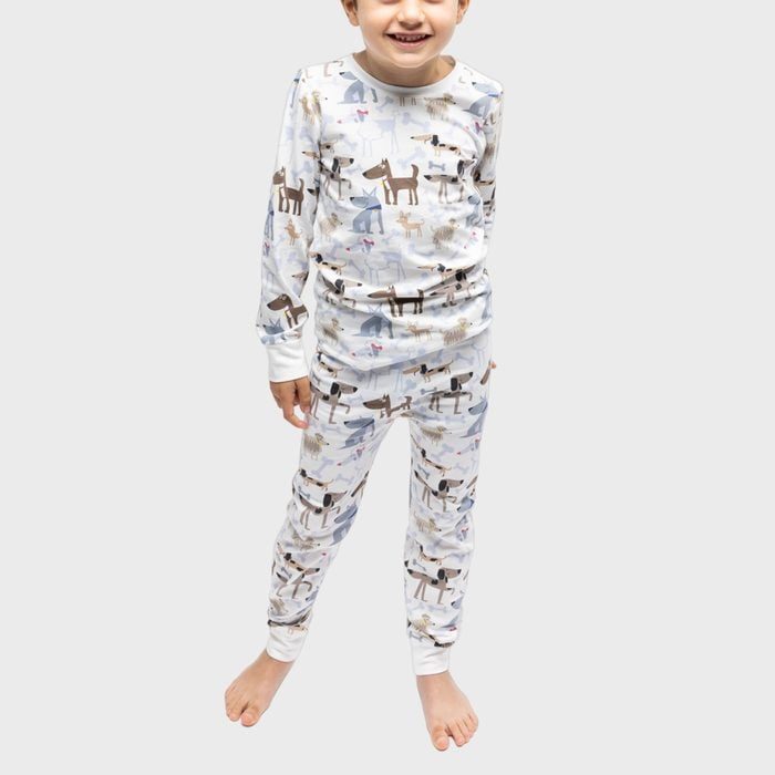 Child wears animal-patterned pajamas, smiling, standing barefoot on a plain, light gray background.
