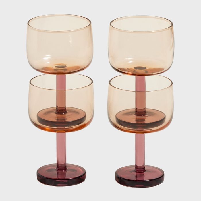 Four stacked, translucent amber wine glasses with pink stems, arranged neatly against a plain light gray background.