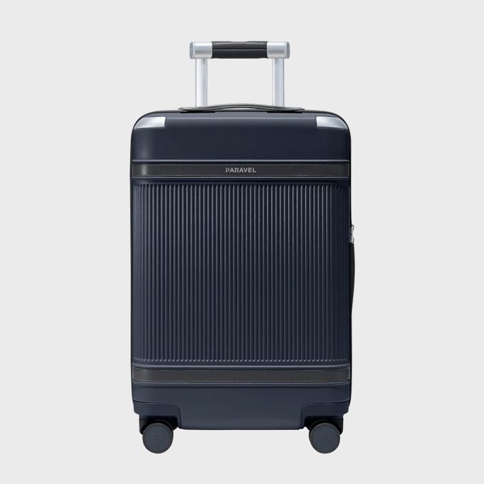 A dark suitcase stands upright with an extended handle and four wheels, set against a plain gray background.