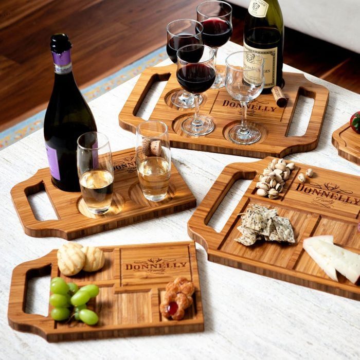 Wooden serving boards display wine glasses, snacks, and bottles on a white table in a cozy room. 
