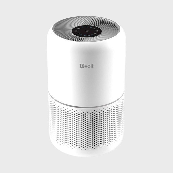 Air purifier resting on a plain background, displaying control buttons on top. The label â€œlevoitâ€ is visible on its cylindrical, perforated surface.